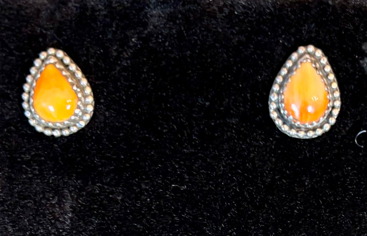 Teardrop-shaped earrings with orange centers and silver borders on a black background