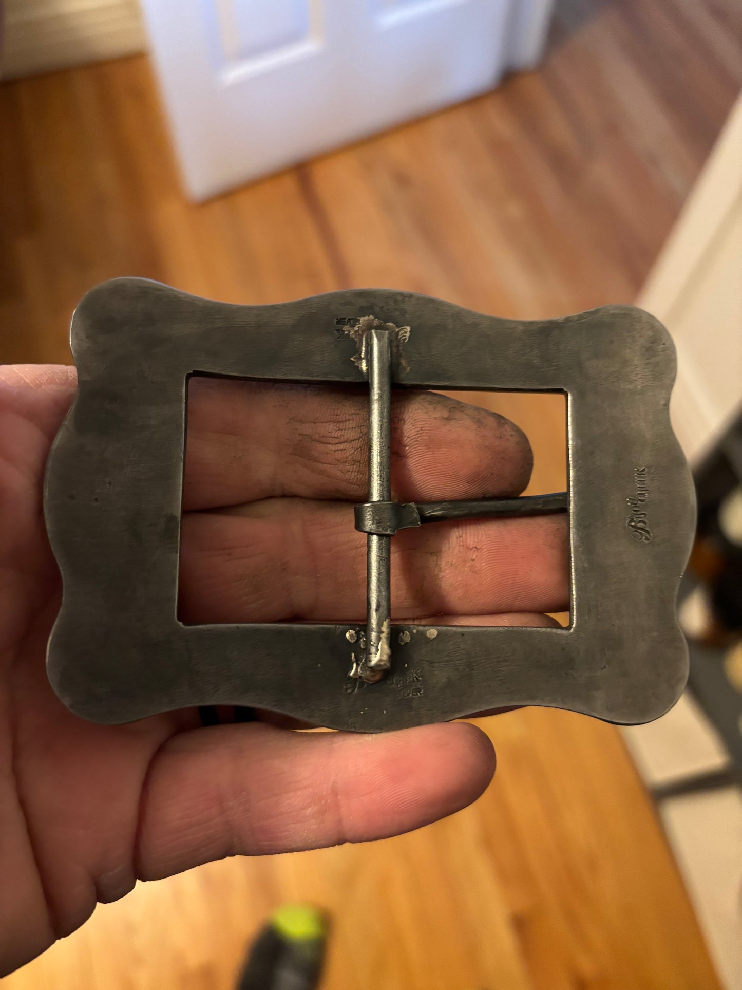 Metal belt buckle held in a hand on a wooden floor