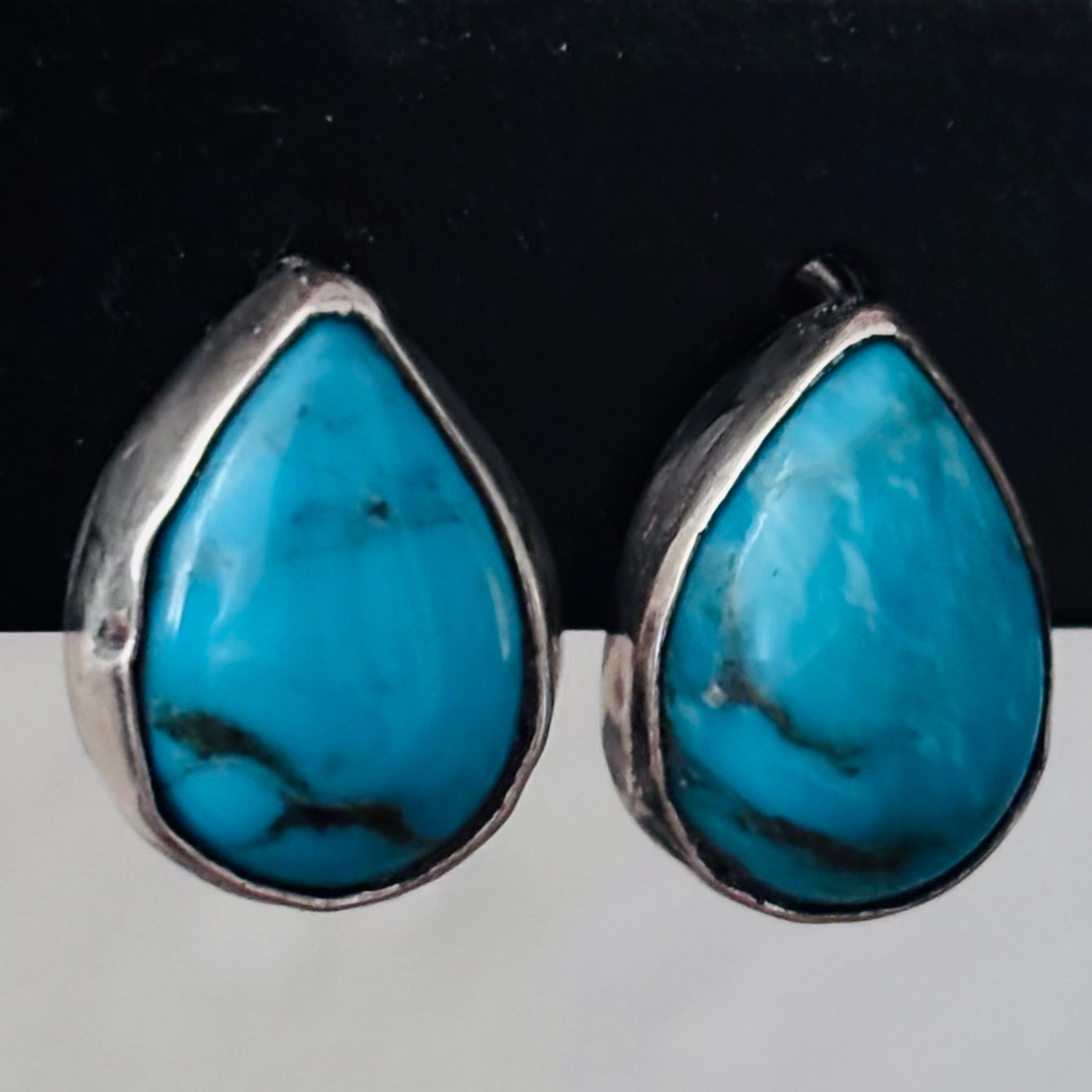 Teardrop-shaped turquoise earrings with silver frames on a black background