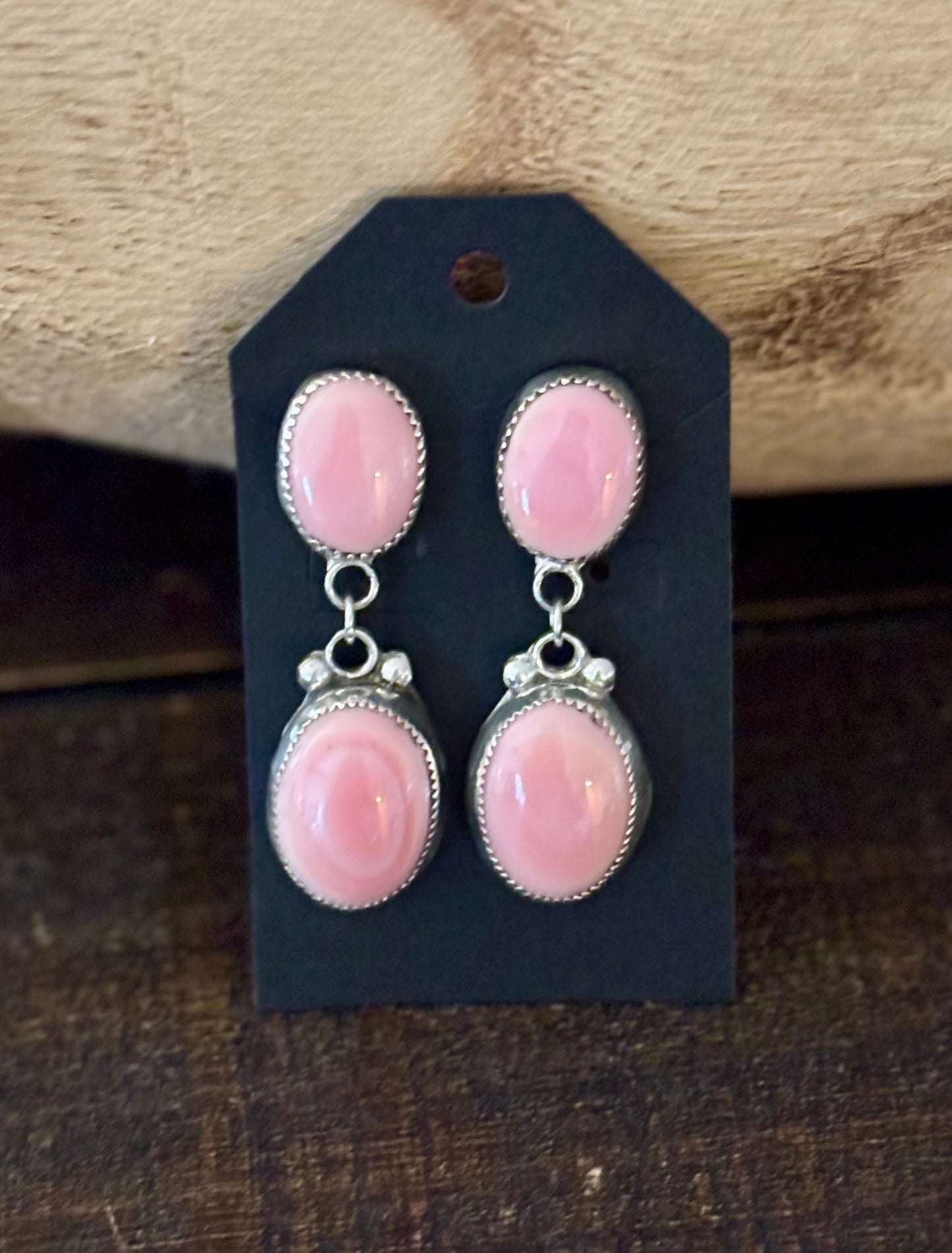 Pair of pink earrings on a black card with a wooden background