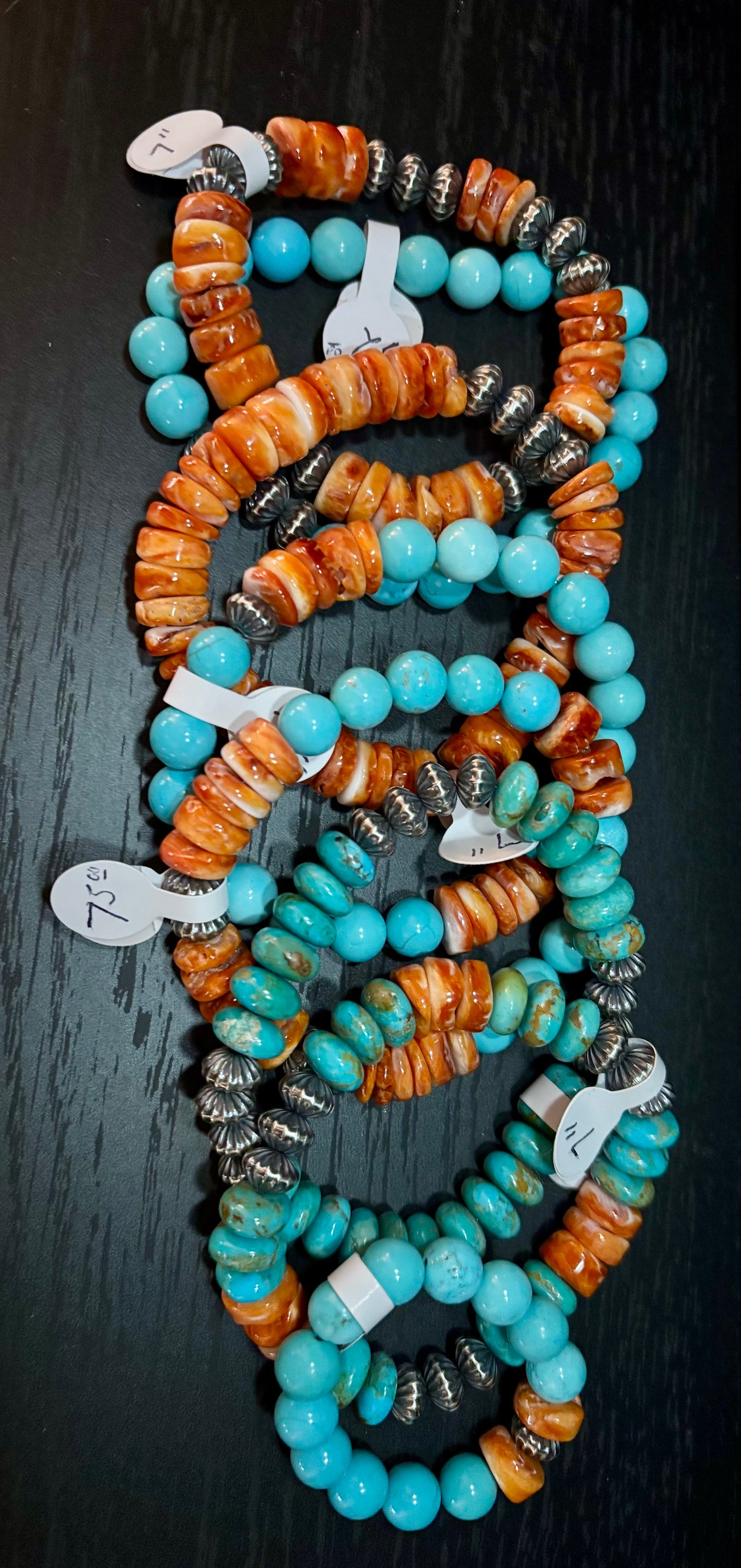 Stack of turquoise and orange beaded necklaces on a dark surface