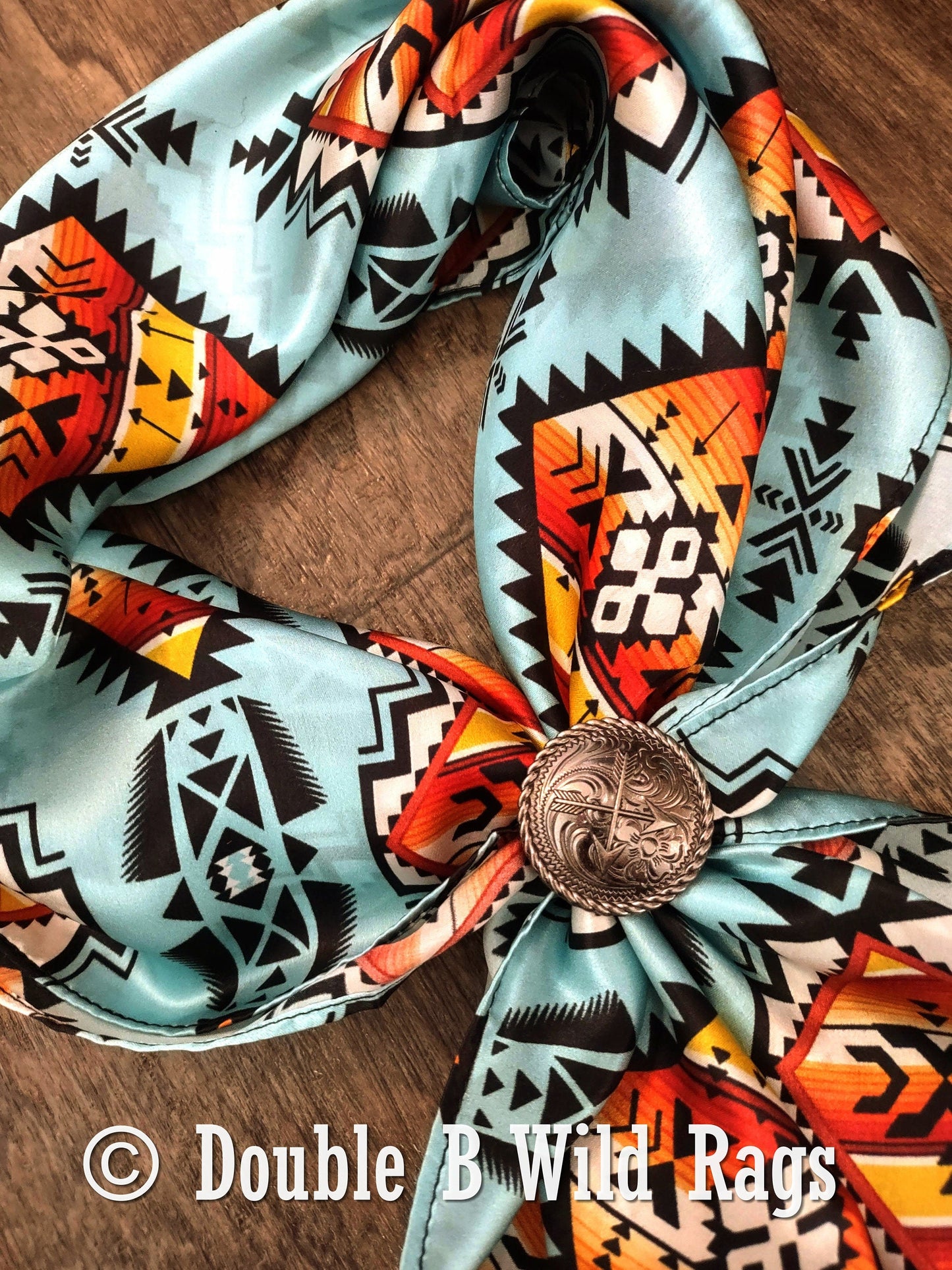 Colorful patterned scarf with a decorative button on a wooden surface, branded 'Double B Wild Rags'.