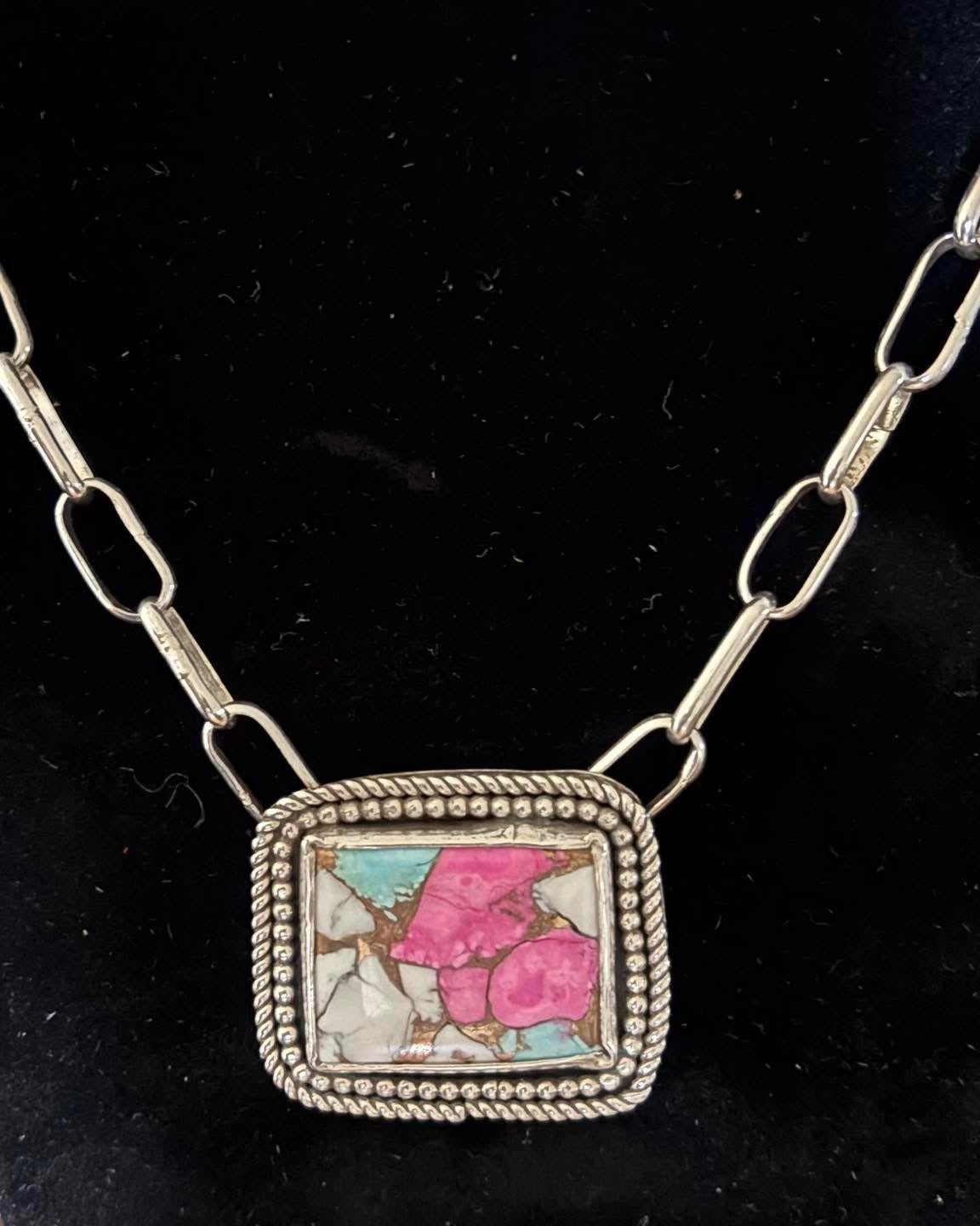 Necklace with a square pendant featuring pink and blue colors on a black background