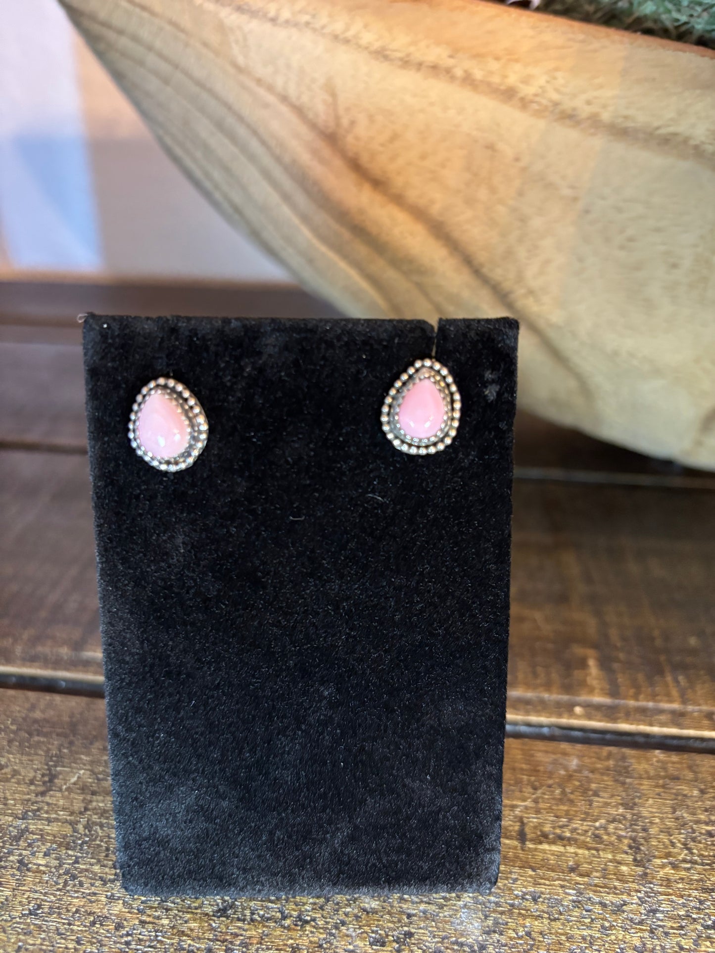 Pair of earrings on a black velvet stand with a pink gemstone, against a wooden background.