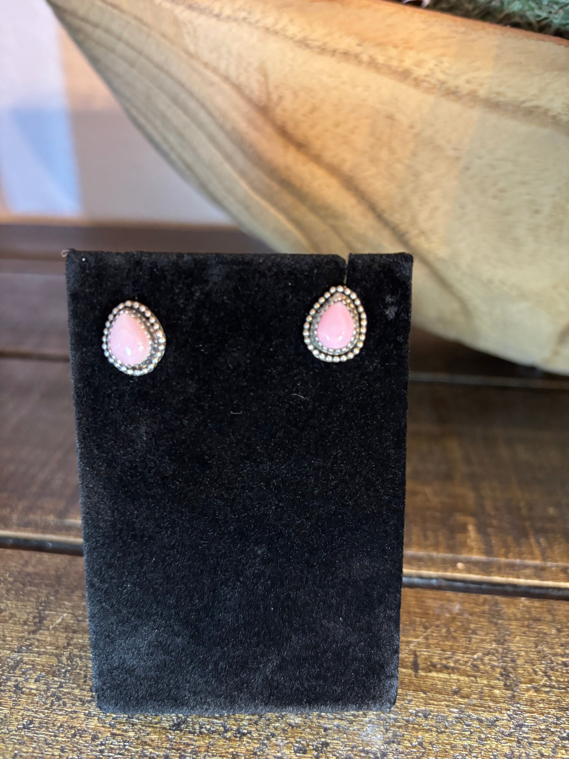 Pair of earrings on a black velvet stand with a pink gemstone, against a wooden background.
