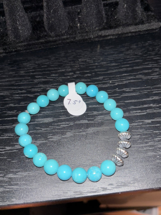 Turquoise beaded bracelet with a silver tag on a dark wooden surface