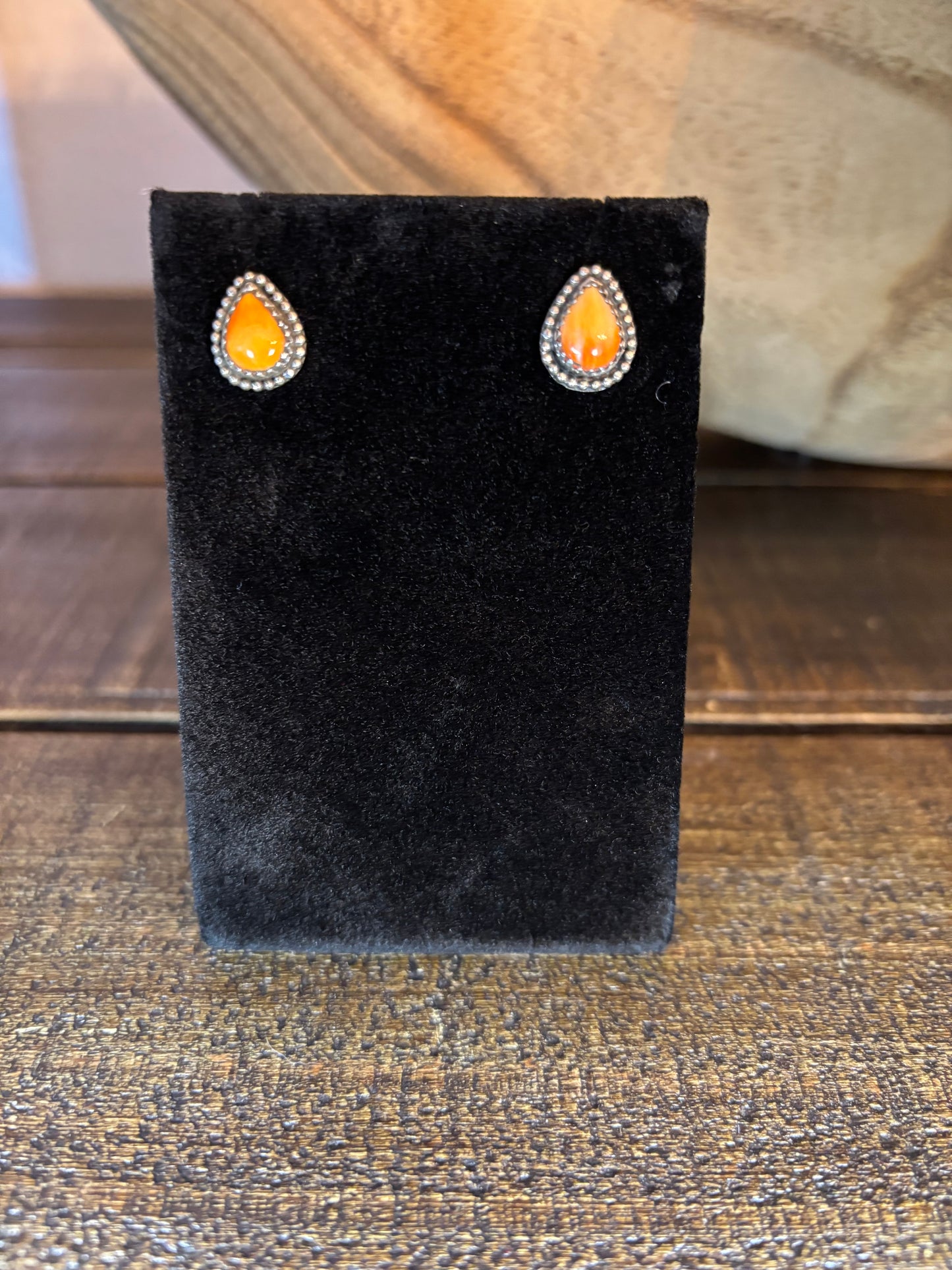 Pair of earrings on a black display stand against a wooden background