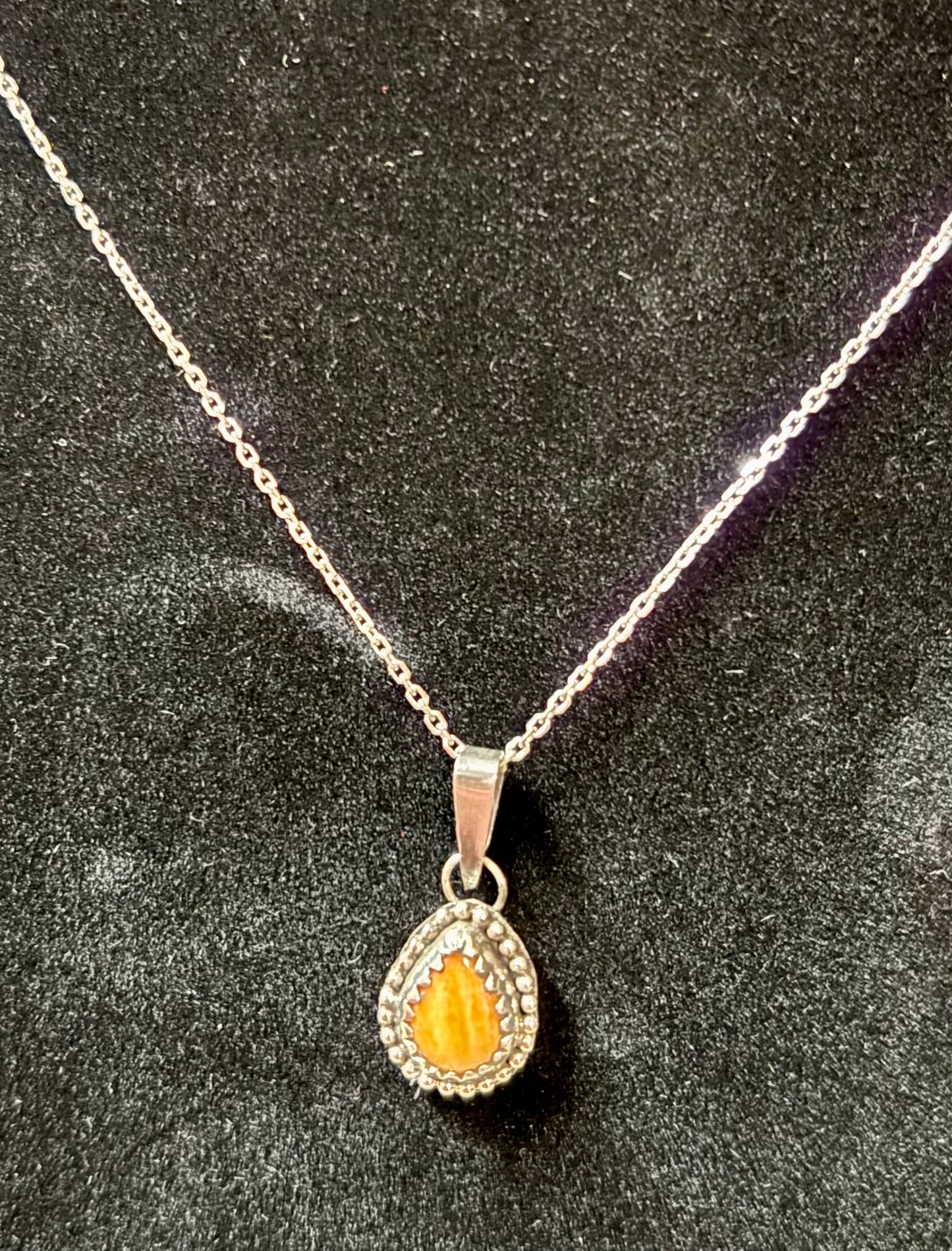 Silver necklace with a teardrop-shaped pendant on a dark textured background