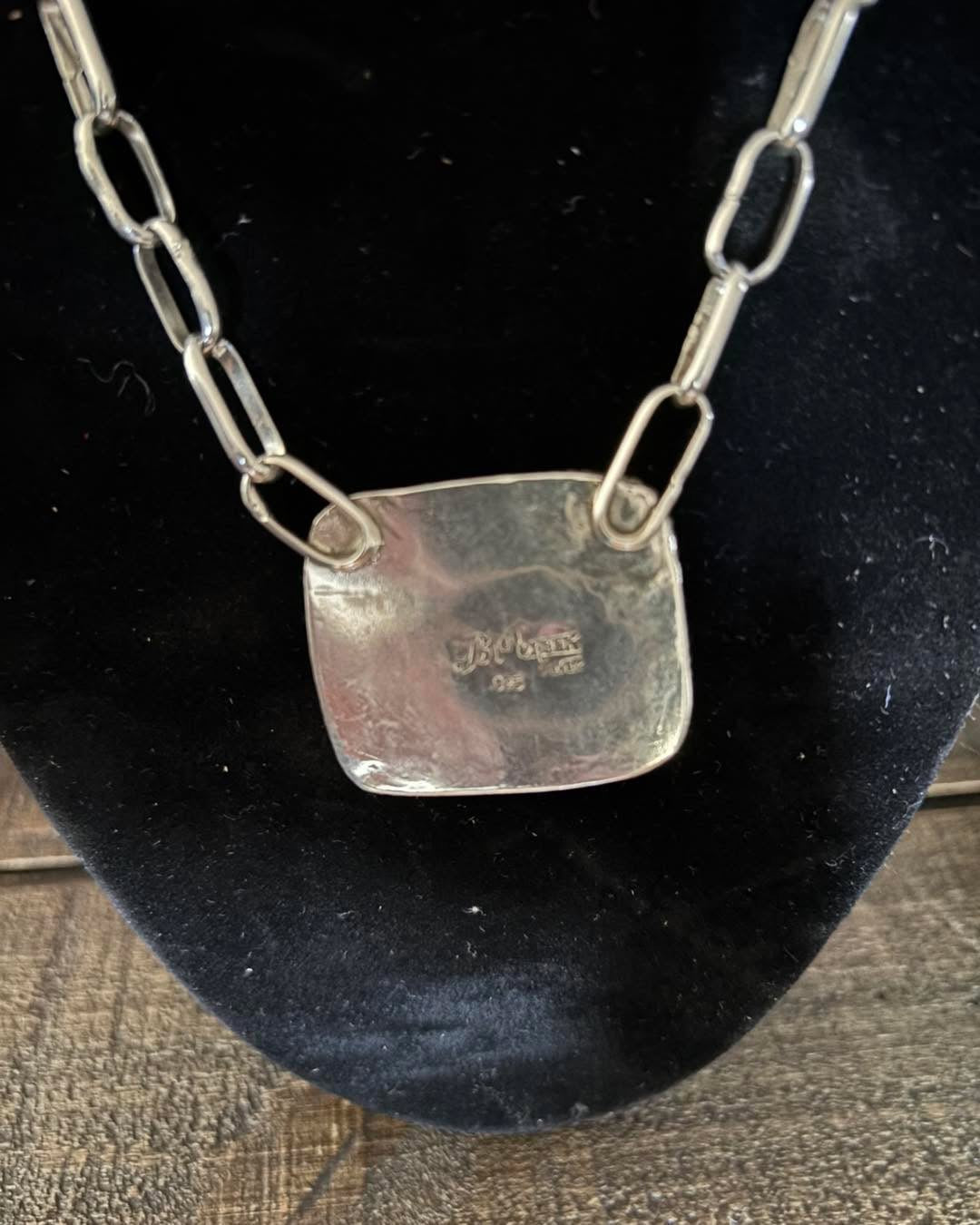 Silver necklace with a square pendant on a black background
