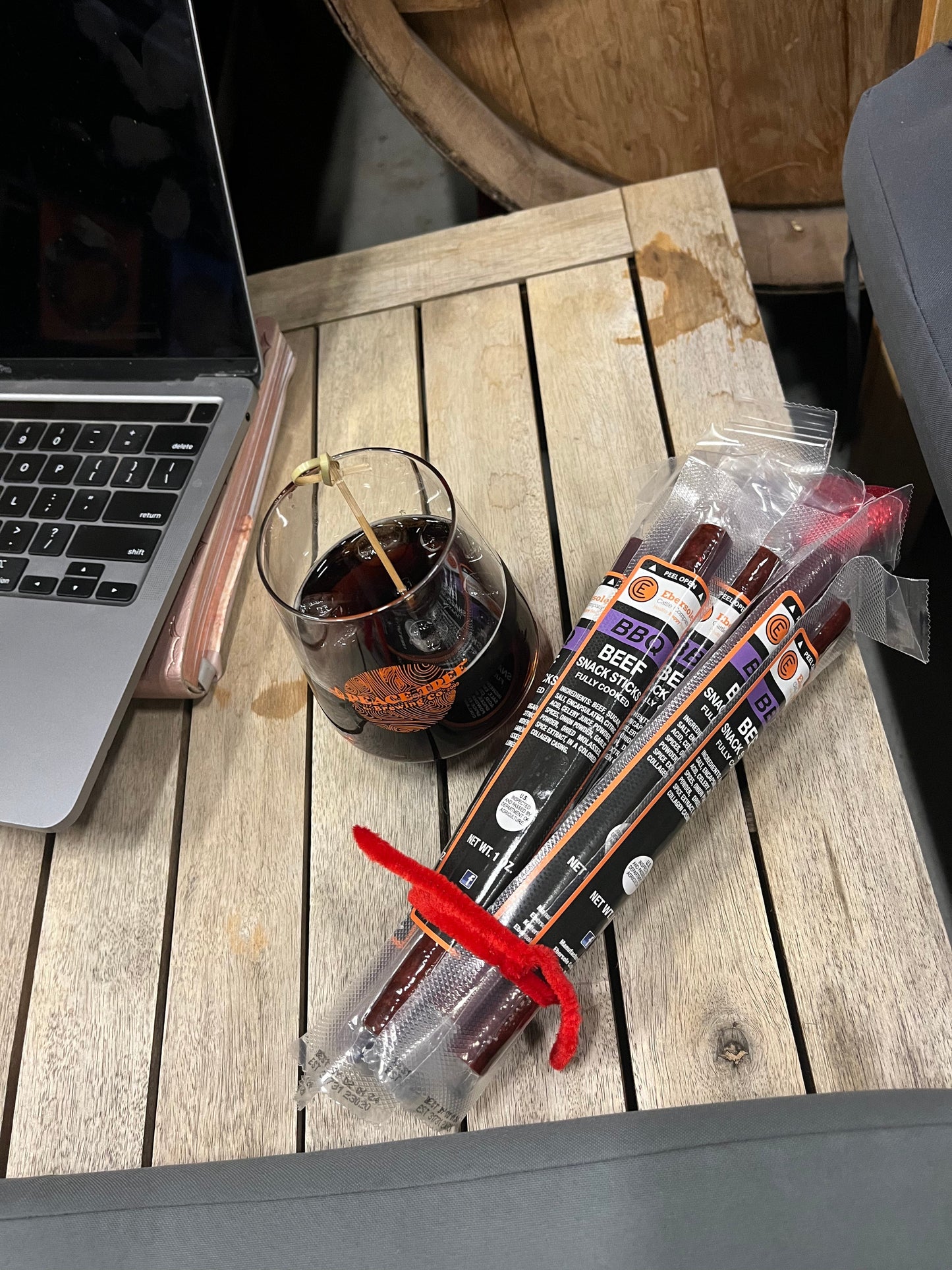 Laptop, glass of dark liquid, and packages of beef jerky on a wooden surface.