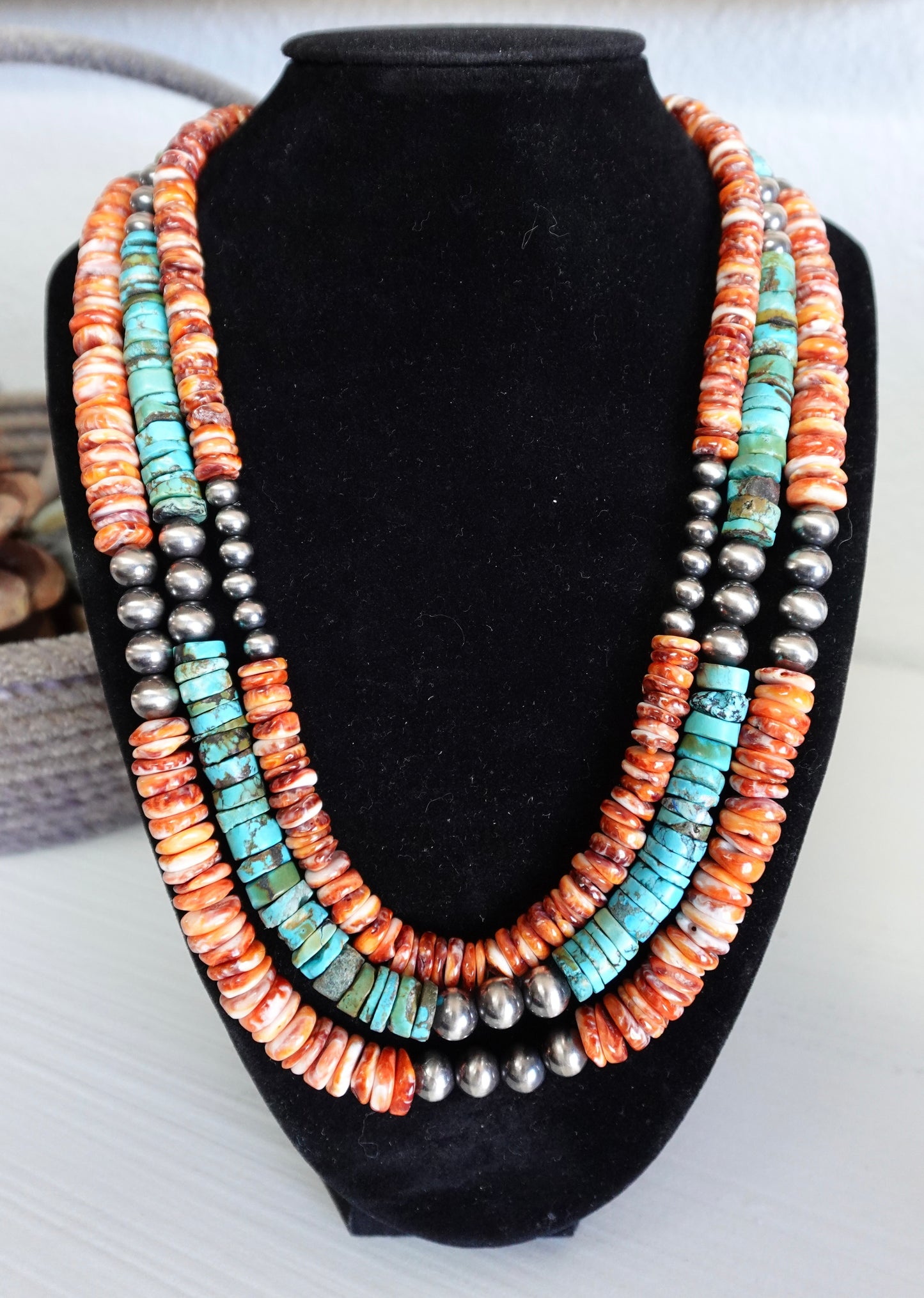 Multistrand necklace with turquoise, coral, and silver beads on a black stand.