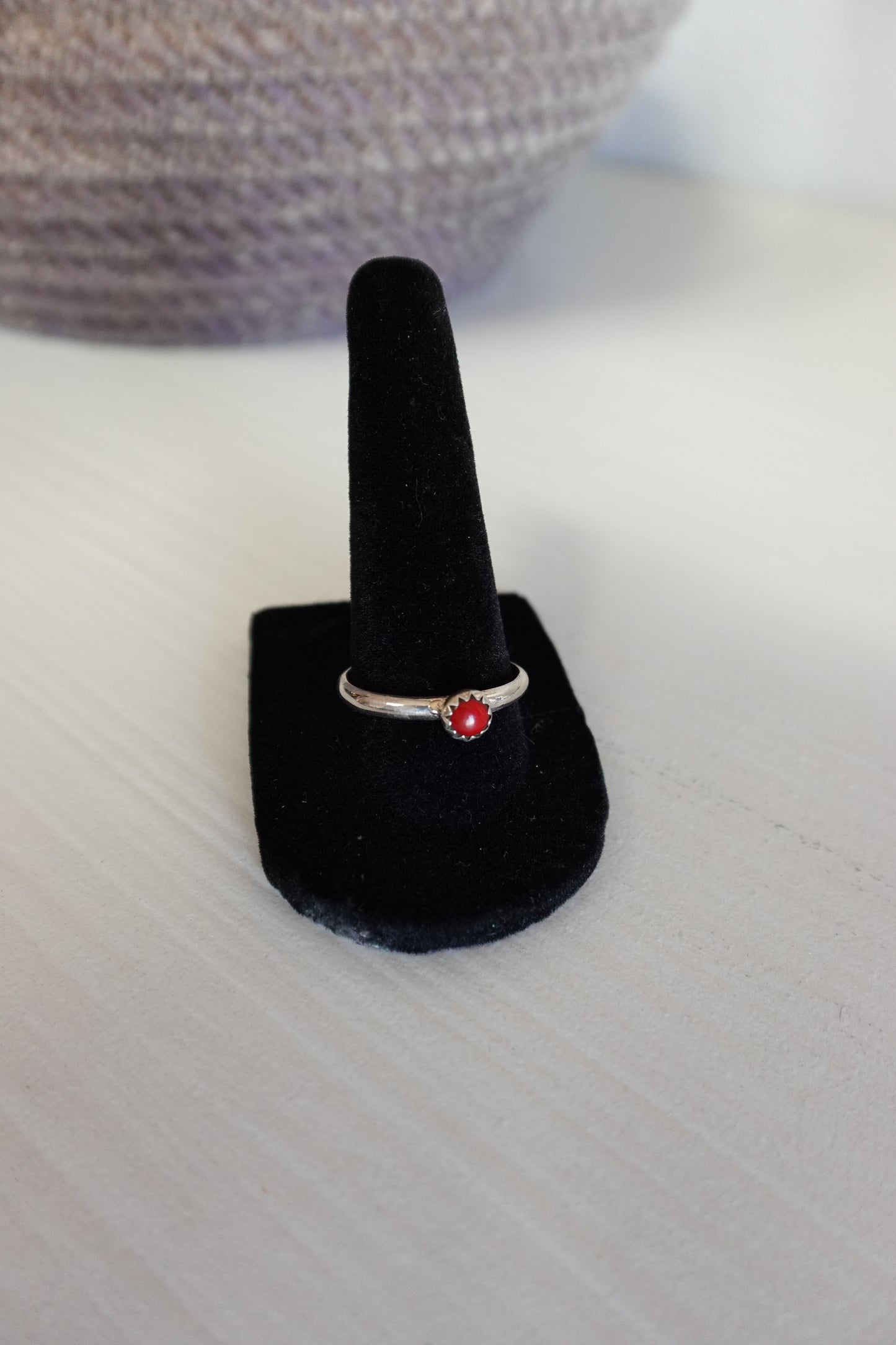 Ring with a red gemstone on a black velvet stand against a neutral background