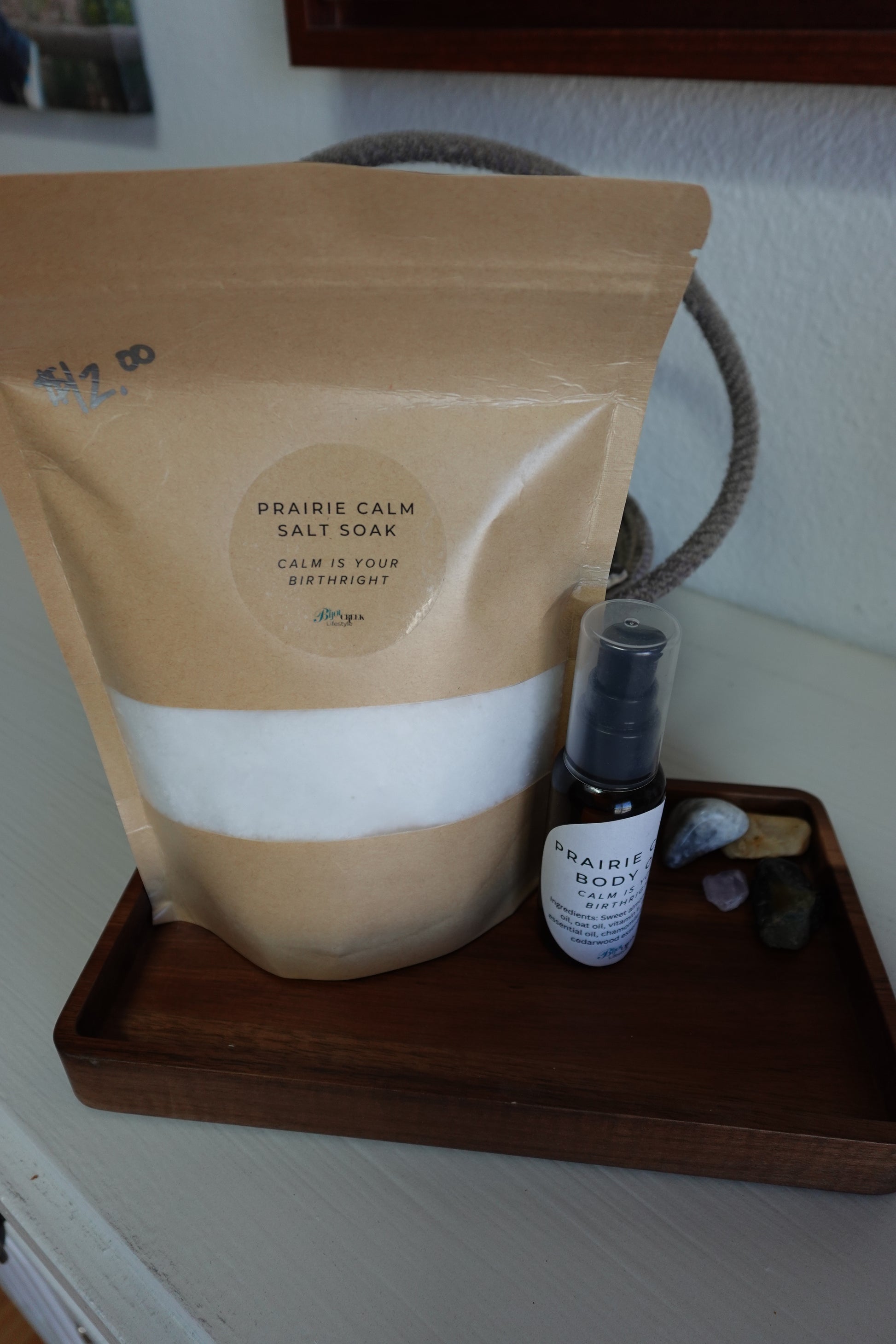 Bottle of Prairie Calm body oil on a wooden tray with a a bag of Prairie Calm Salt Soak