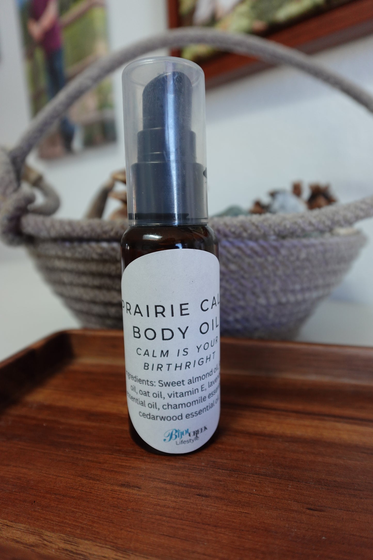 Bottle of Prairie Calm Body Oil on a wooden tray with a rope basket in the background