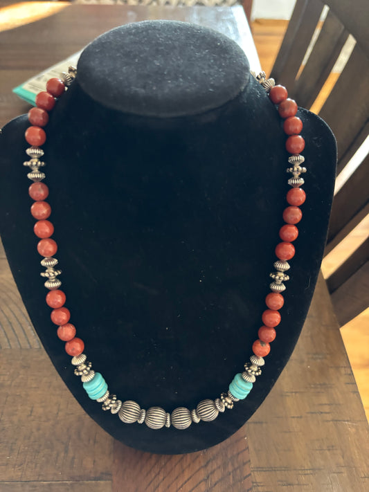 Necklace with red, turquoise, and silver beads on a black stand.