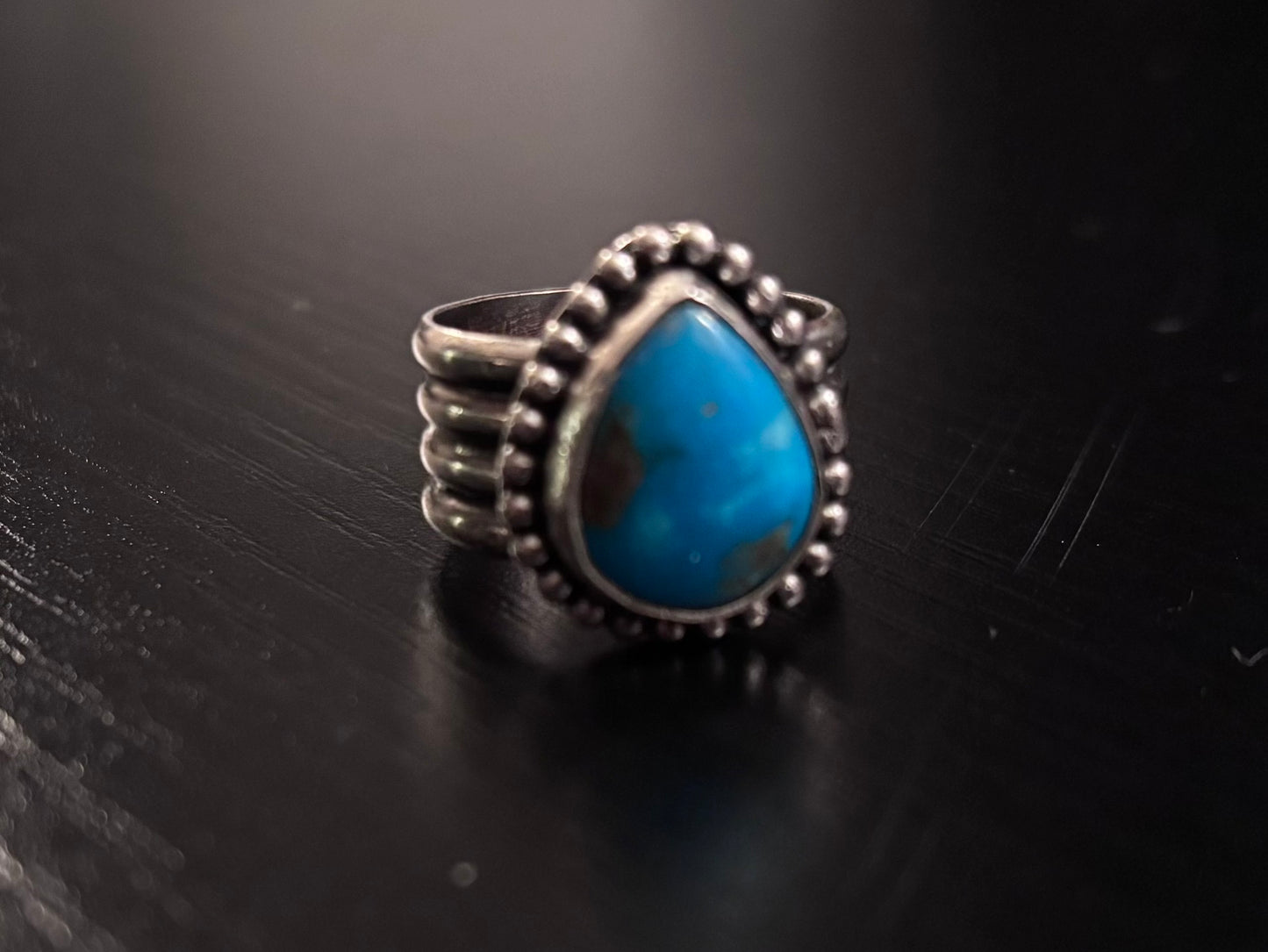 Silver ring with a blue stone on a black surface