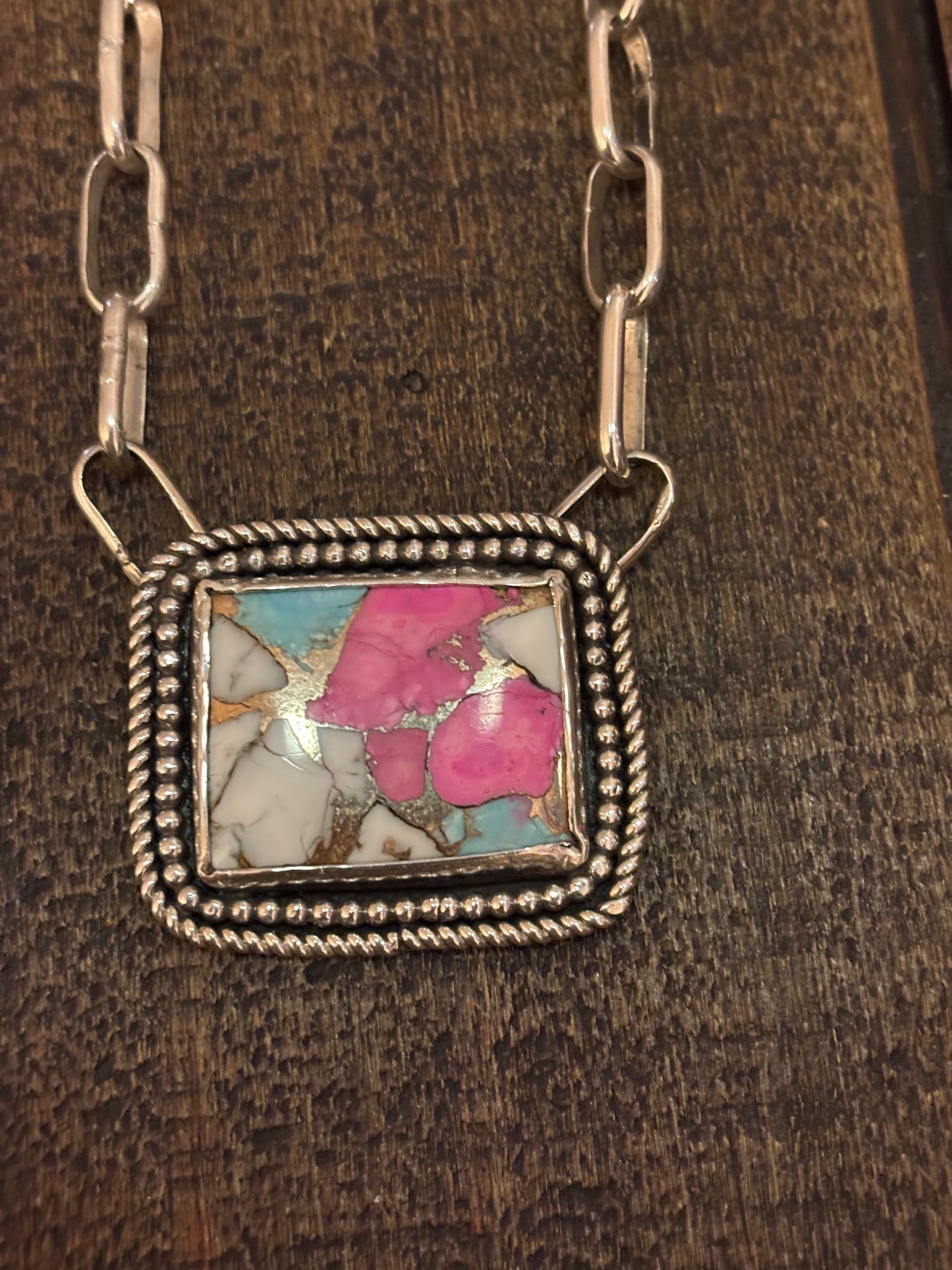 Necklace with a square pendant featuring a colorful stone on a wooden surface