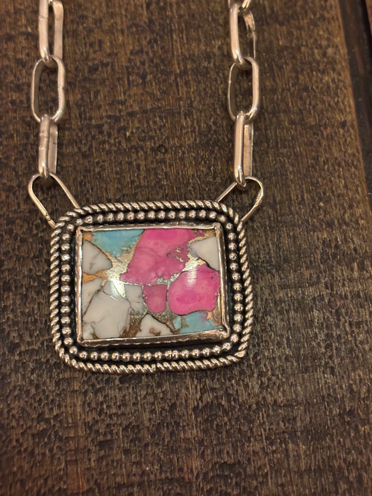 Necklace with a square pendant featuring a colorful stone on a wooden surface
