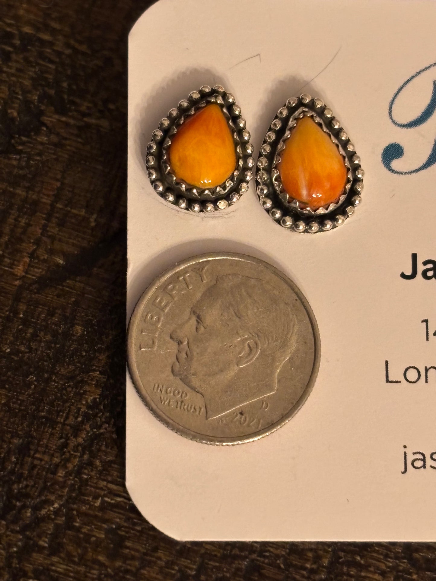 Teardrop-shaped earrings with orange stones on a card next to a coin for scale.