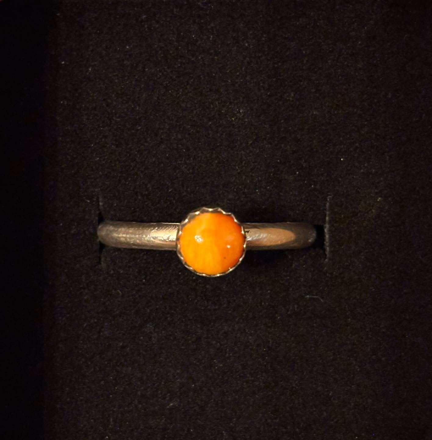 Silver ring with an orange stone on a black background