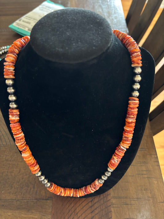 Necklace with orange and silver beads on a black velvet stand.