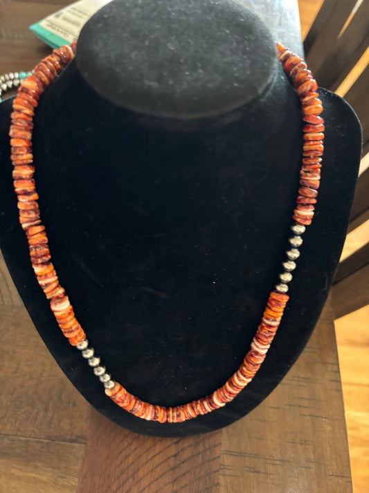 Necklace with orange and silver beads on a black mannequin bust.