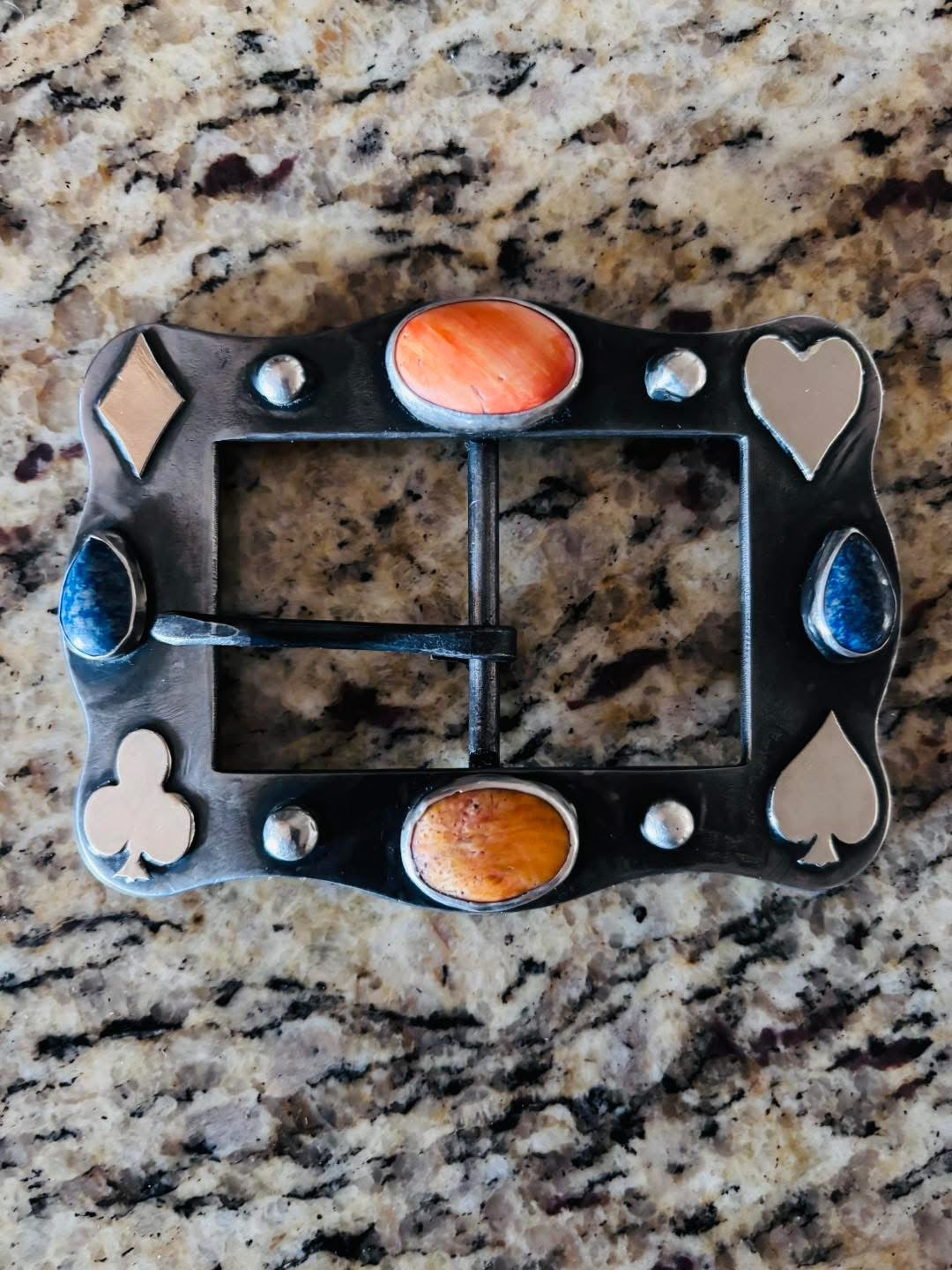 Decorative belt buckle with card suit symbols on a marble surface