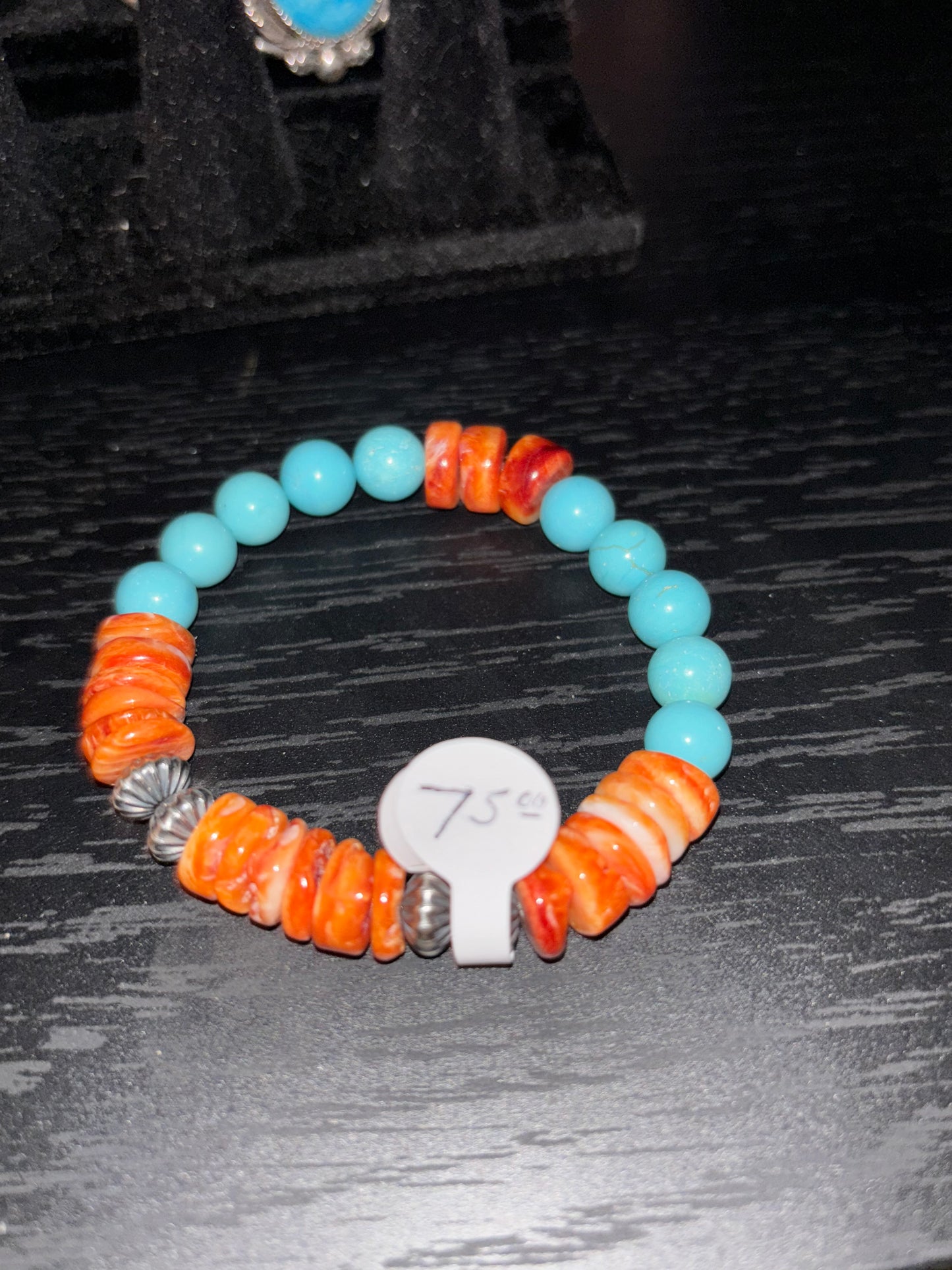 Beaded bracelet with orange, blue, and silver beads on a dark textured surface