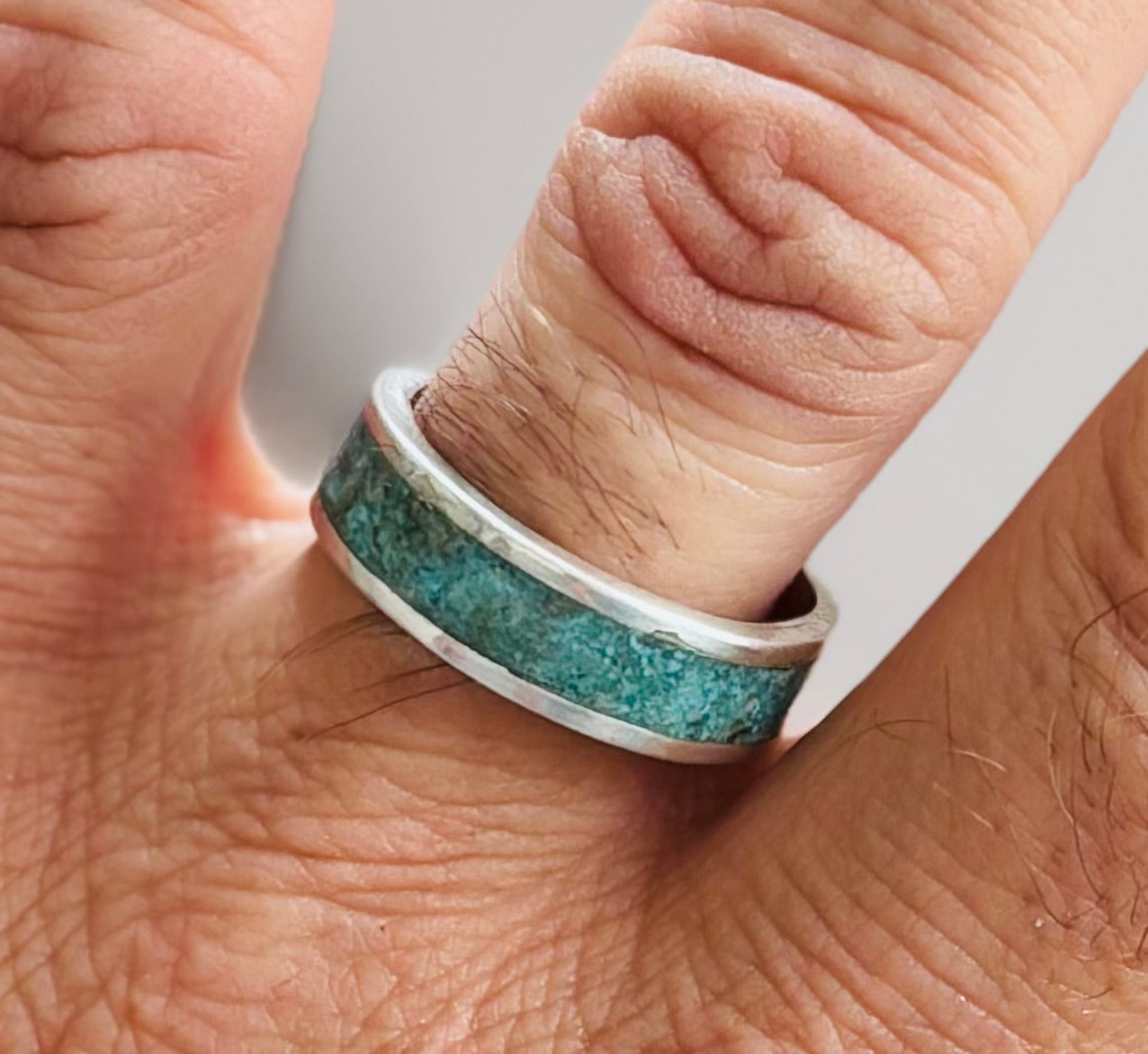 Close-up of a hand wearing a ring with a turquoise band and silver edge.