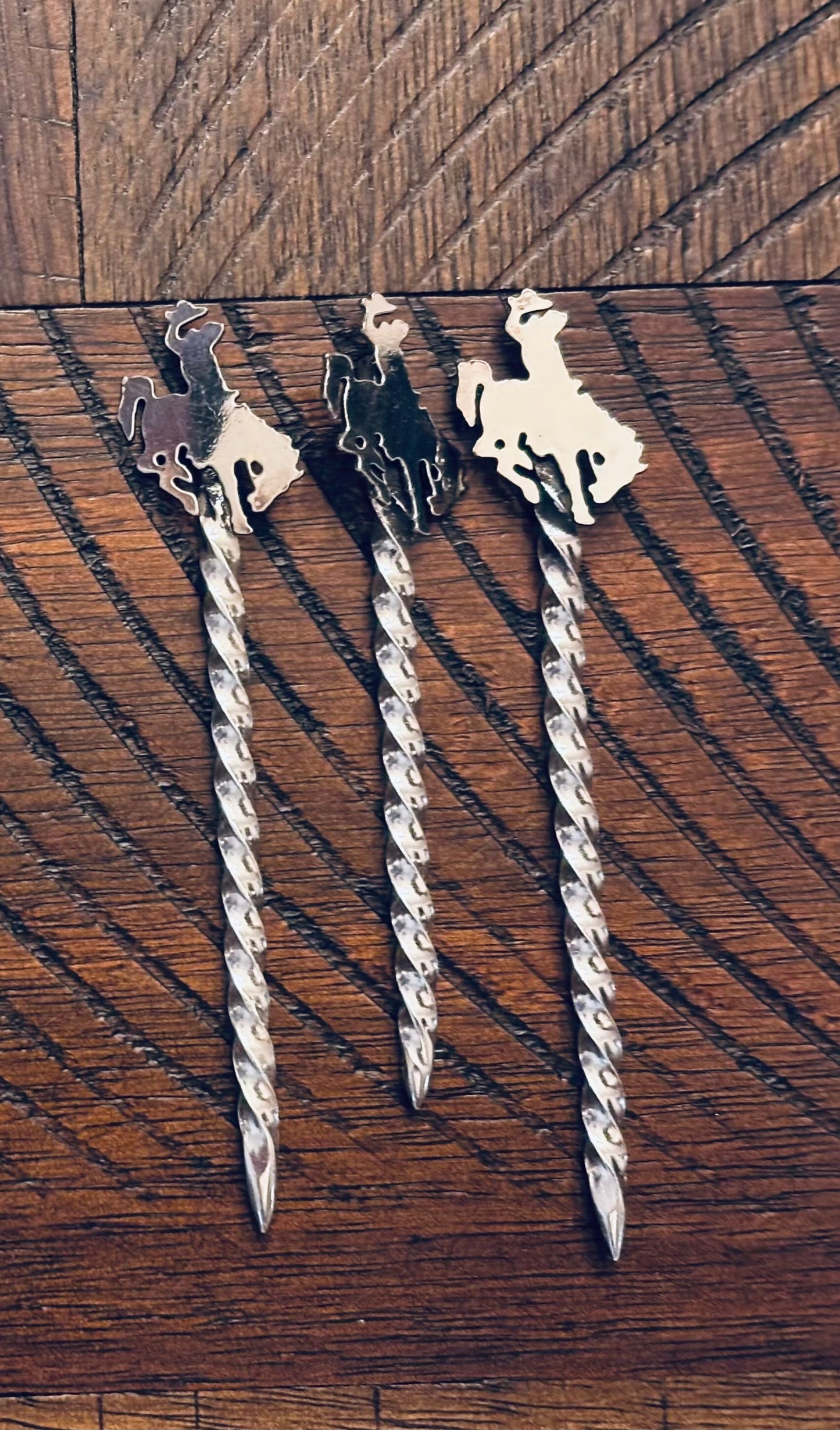 Three decorative hair pins with horse designs on a wooden surface