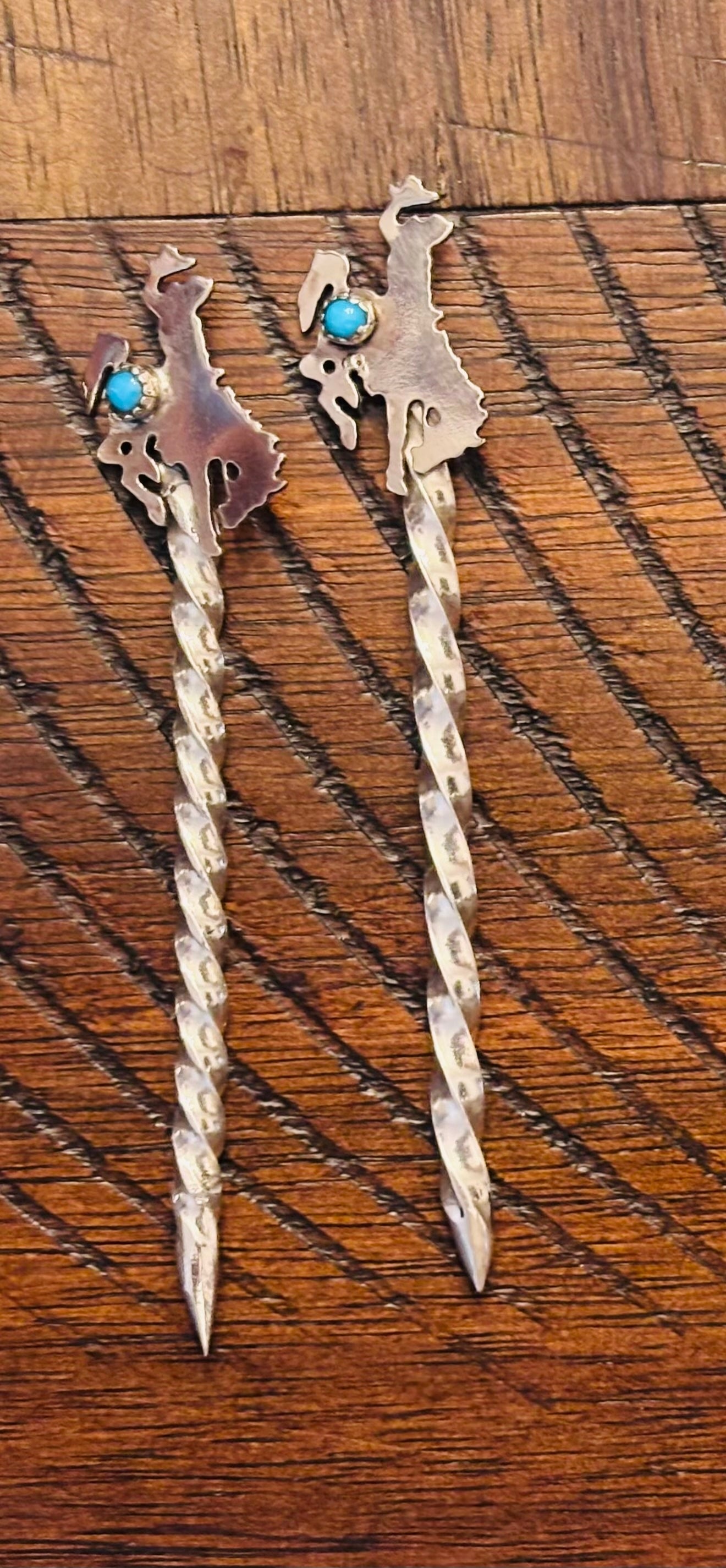 Pair of silver hair sticks with turquoise stones on a wooden surface