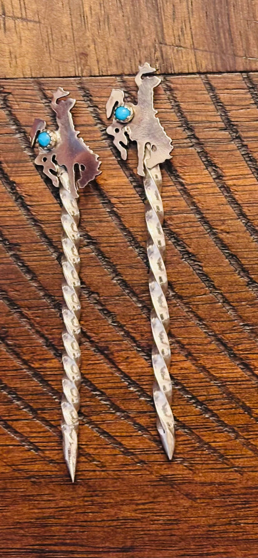 Pair of silver hair sticks with turquoise stones on a wooden surface