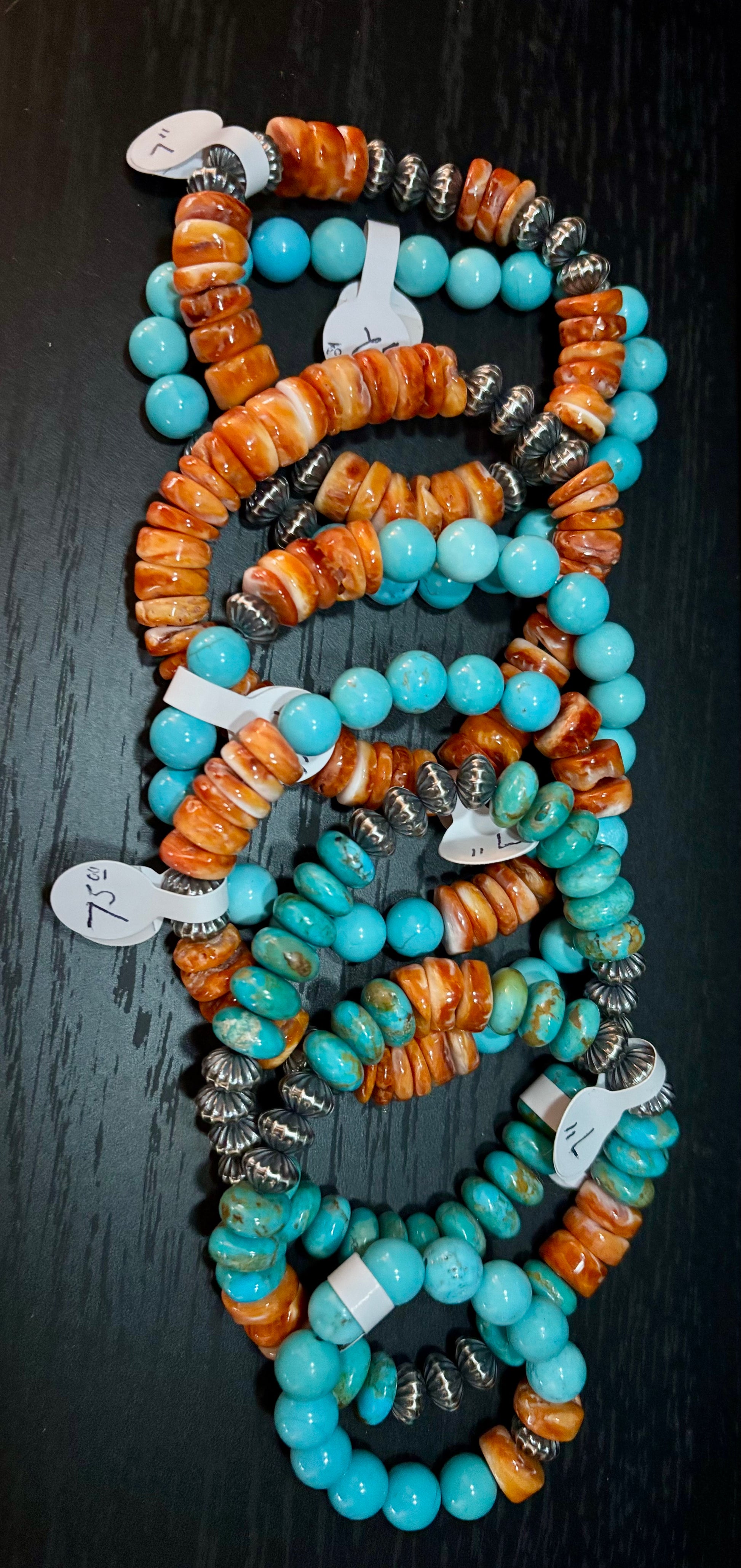 Stack of turquoise and orange beaded necklaces on a dark surface
