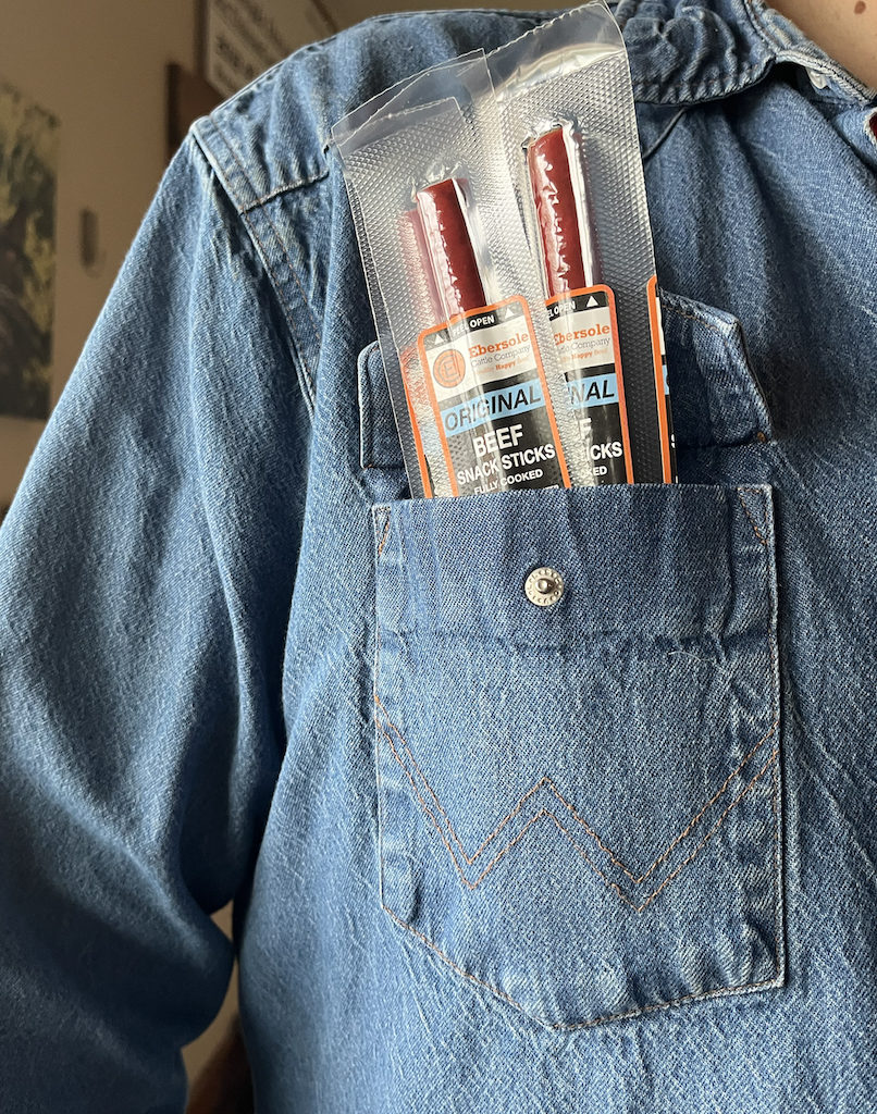 Two packages of beef stick snacks in a blue denim pocket.