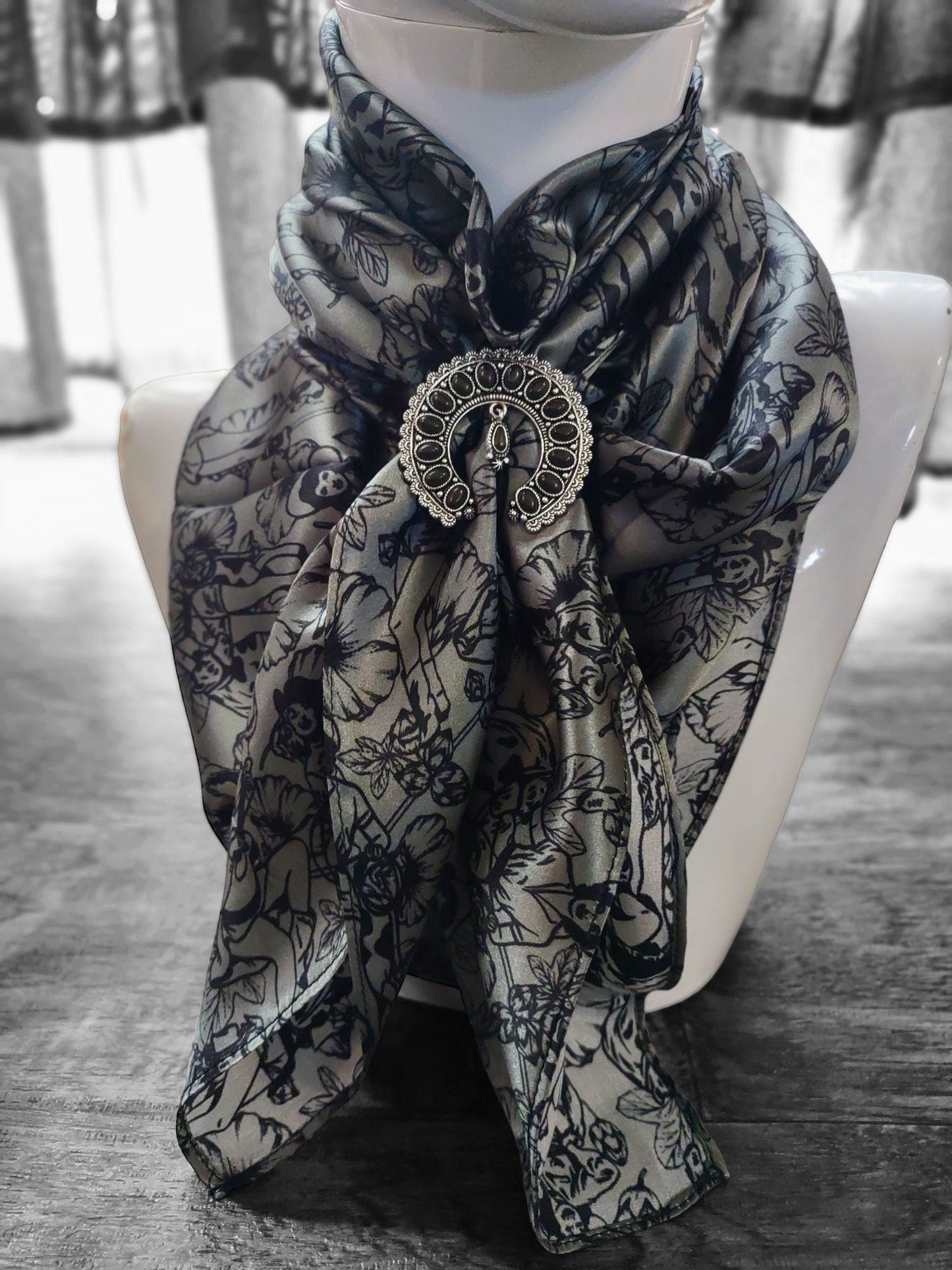 Scarf with decorative brooch on a mannequin against a blurred indoor background