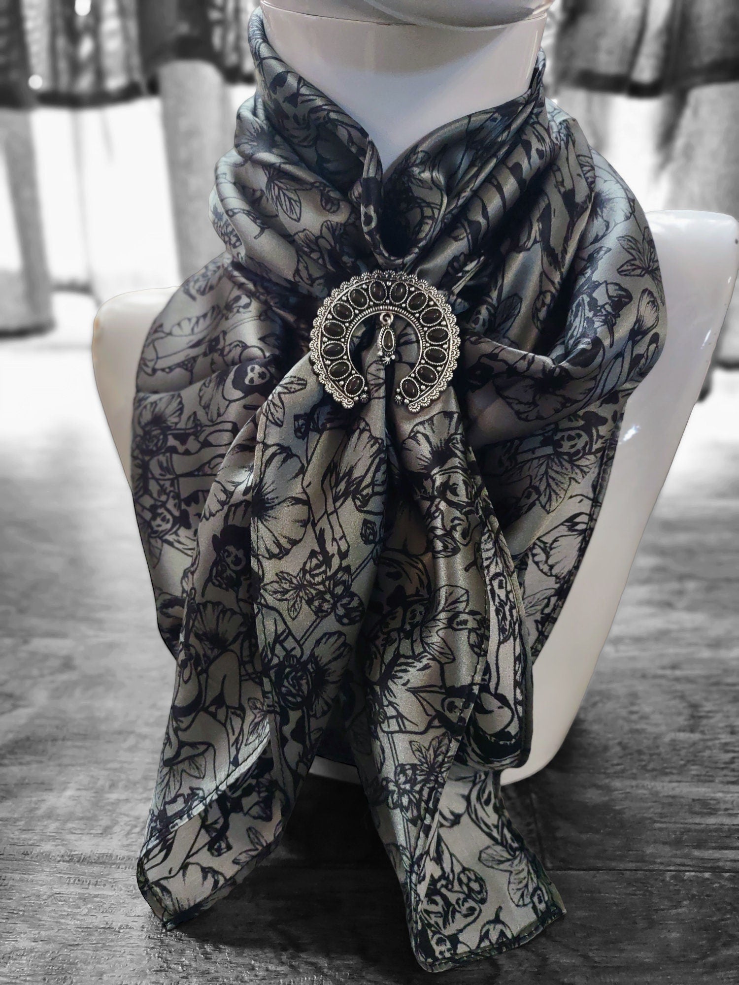 Scarf with decorative brooch on a mannequin against a blurred indoor background