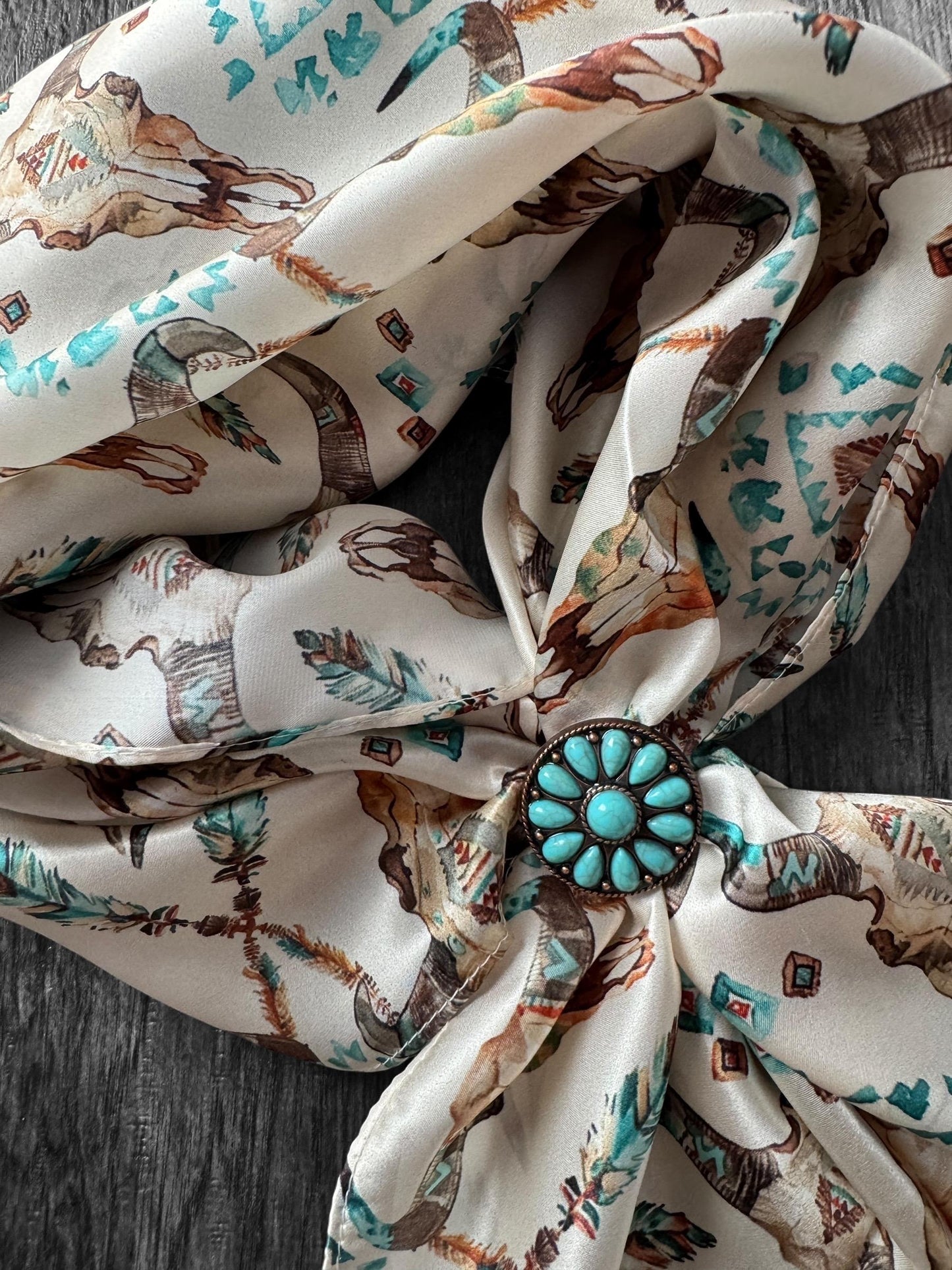 Scarf with horse print and turquoise brooch on a wooden surface