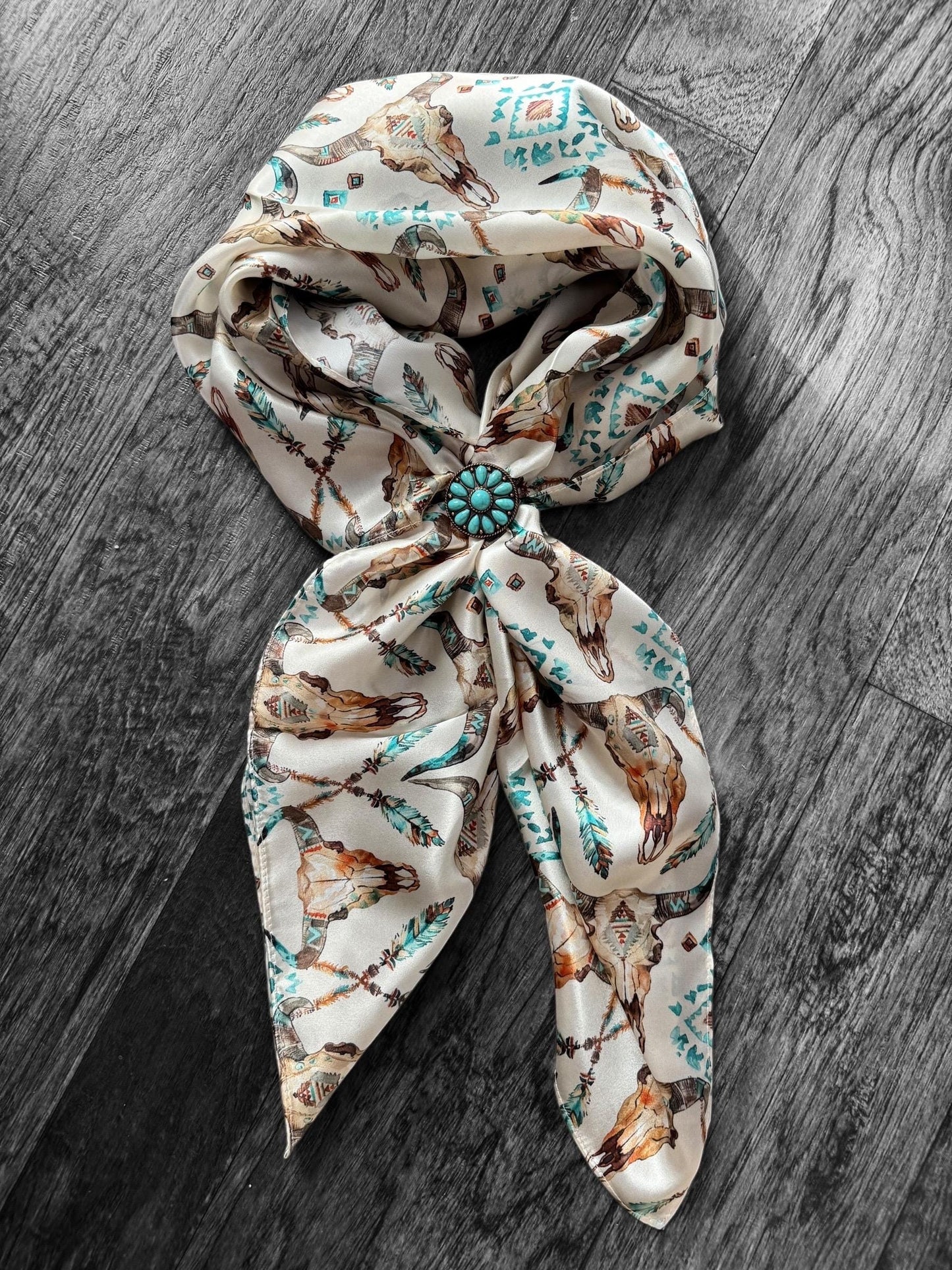 Decorative headscarf with a floral pattern and turquoise brooch on a wooden surface